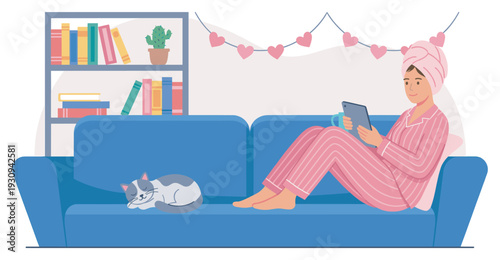 Young woman relaxes comfortably on her blue couch while reading on a tablet with her sleeping cat nearby, enjoying a cozy evening at home.