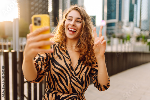 Φωτογραφία A smiling woman with phone in hand is blogging or videoconferencing against backdrop of metropolis