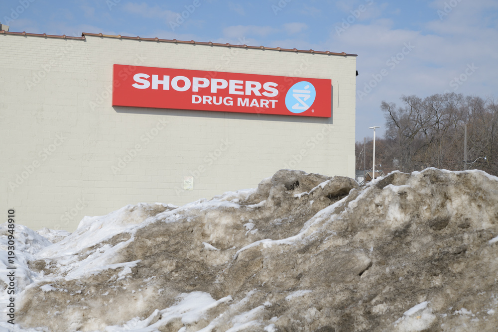 Obraz premium grungy snow pile and wall mounted sign outside Shoppers Drug Mart a pharmacy chain located here at 265 Coxwell Av (seen from Gerrard St E), Toronto