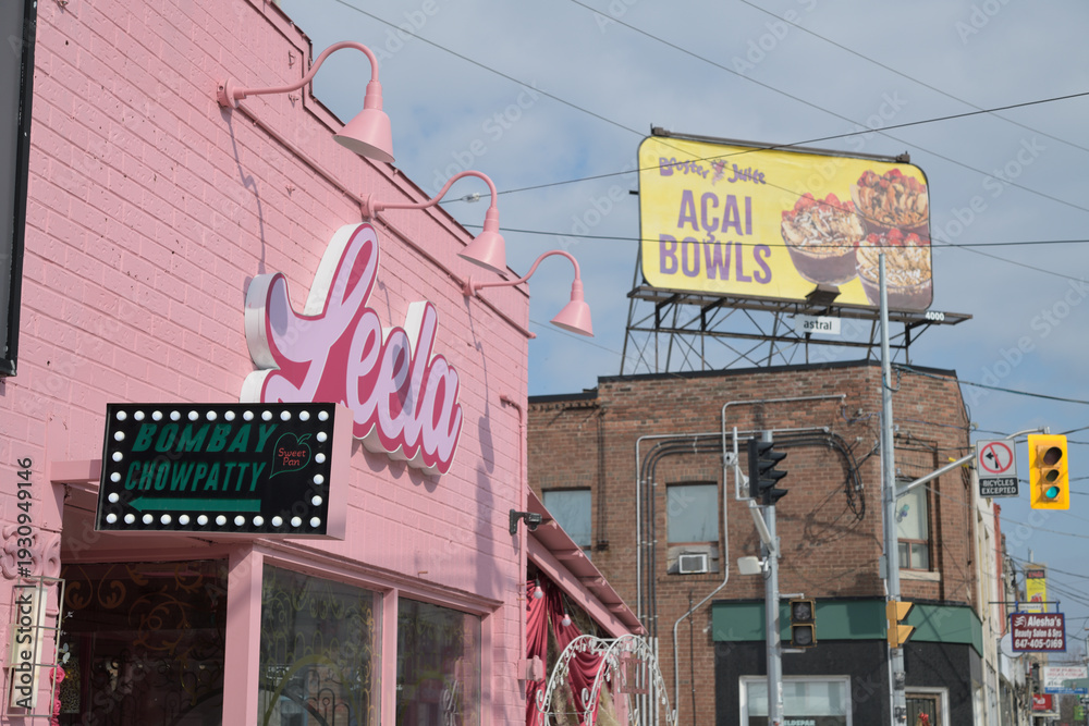 Fototapeta premium looking east on Gerrard St E with view of Leela Indian Food Bar at 1386 Gerrard St E, rooftop Booster Juice billboard, and buildings, Toronto