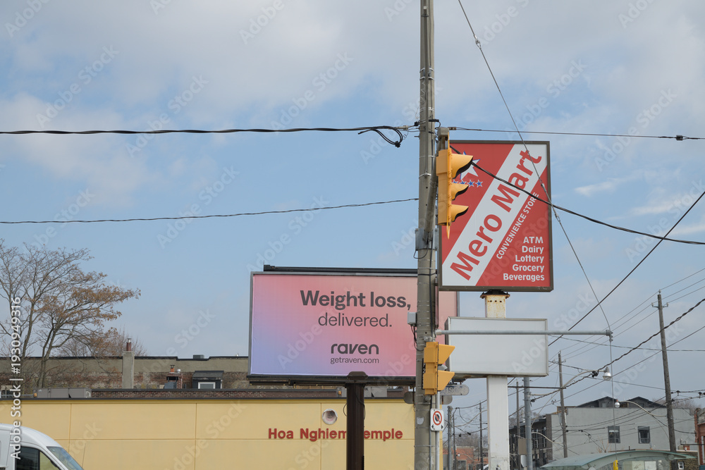 Fototapeta premium looking east on Gerrard St E from about Greenwood Av to signs (Metro Mart, and Raven vitamins) and Hoa Nghiem Temple, a Buddhist temple at 1278 Gerrard St E, Toronto