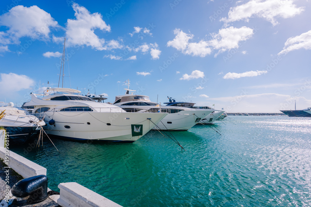 Fototapeta premium Luxury yachts docked at a marina with clear blue waters and a bright sky, showcasing modern boat designs and nautical lifestyle