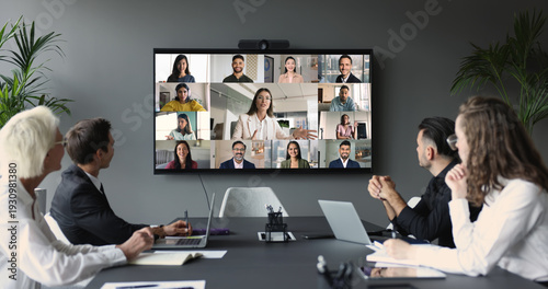 Foto Group of businesspeople gather at conference table collaborating with multiple participants from diverse locations displayed on TV screen, take part in corporate discussion