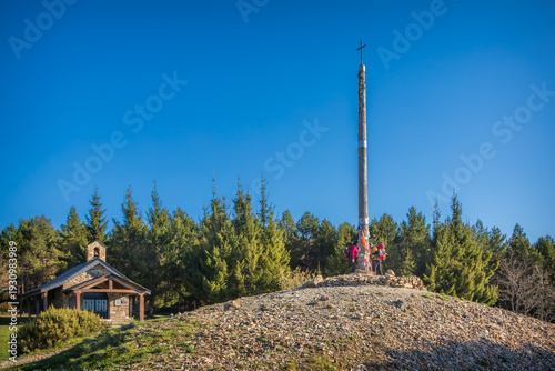 Pilgrims at the famous Cruz de Ferro Iron Cross on a mound of stones near a small chapel on the Camino de Santiago, a symbolic site for spiritual reflection in the Leon mountains of northern Spain