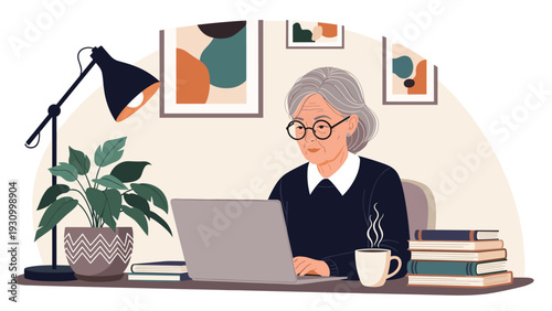Senior woman with gray hair and glasses works on a laptop at a desk with a plant cup of coffee and stacks of books in a home office.