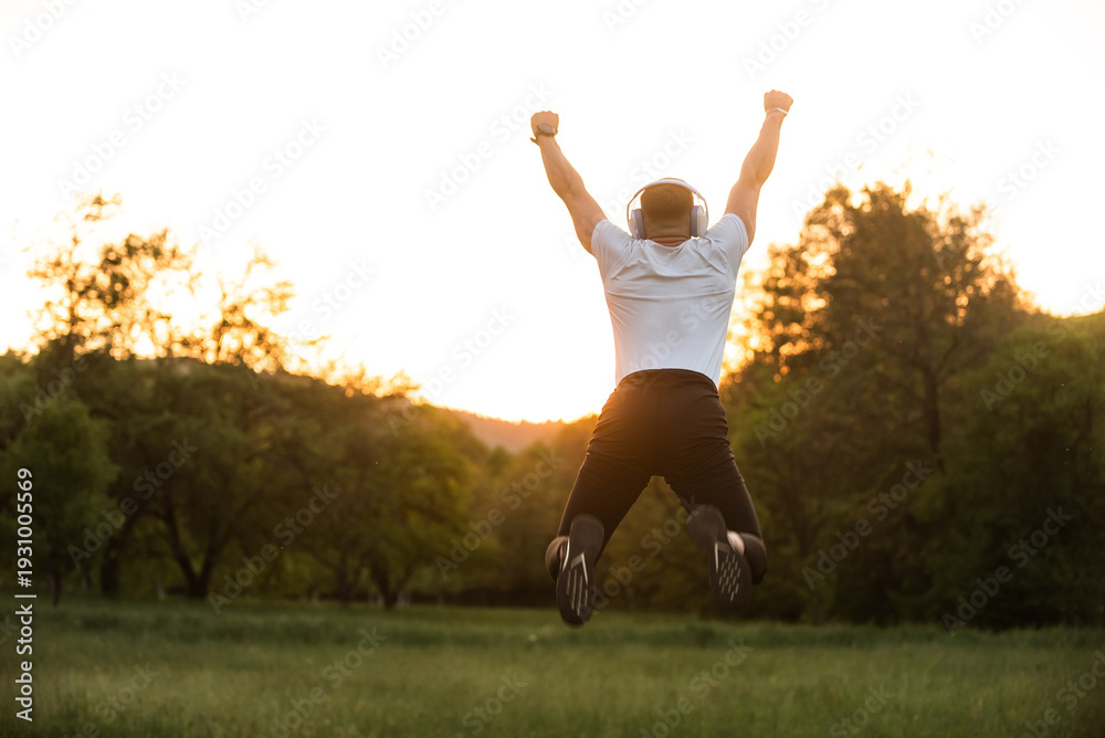 Fototapeta premium Success And Achievement Fit Man Jumping For Joy With Headphones Outdoors At Sunset Celebrating Freedom Wellbeing And Healthy Lifestyle In Nature Expressing Happiness.