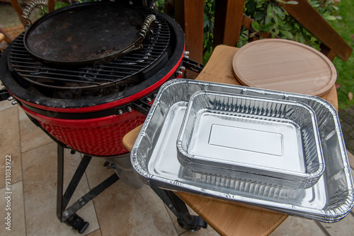 Ceramic grill with disposable aluminum trays on side shelf outdoors