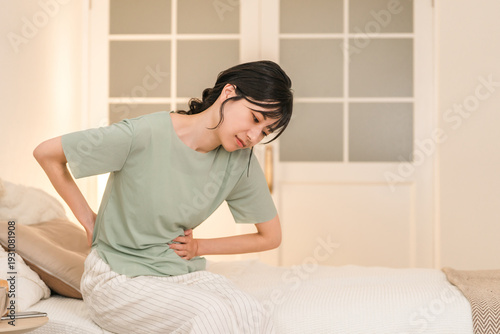 Schilderij op canvas Young Asian woman suffering from abdominal pain and menstrual cramps in her bedr