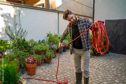 Gardener gathering the hose after watering the plants , closeup shot