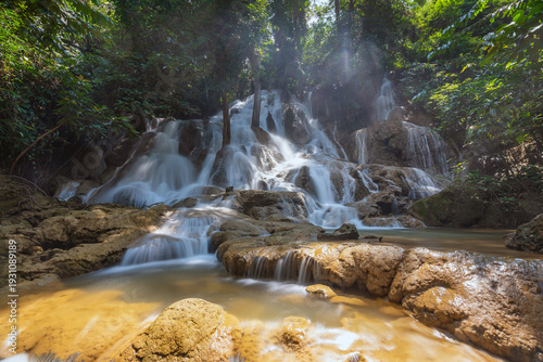 Serene tropical Dai Chong Thong waterfall cascade over limestone rock in lush forest at Sangkhlaburi, Kanchanaburi, Thailand under soft morning light