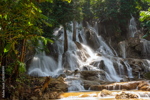 Serene tropical Dai Chong Thong waterfall cascade over limestone rock in lush forest at Sangkhlaburi, Kanchanaburi, Thailand under soft morning light