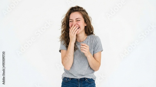 Candid portrait of a joyful young woman in a grey t-shirt laughing heartily and covering her mouth, isolated on a white background