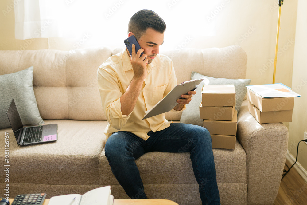 Fototapeta premium Latin man working remotely, handling shipments and customer service for online business from home office