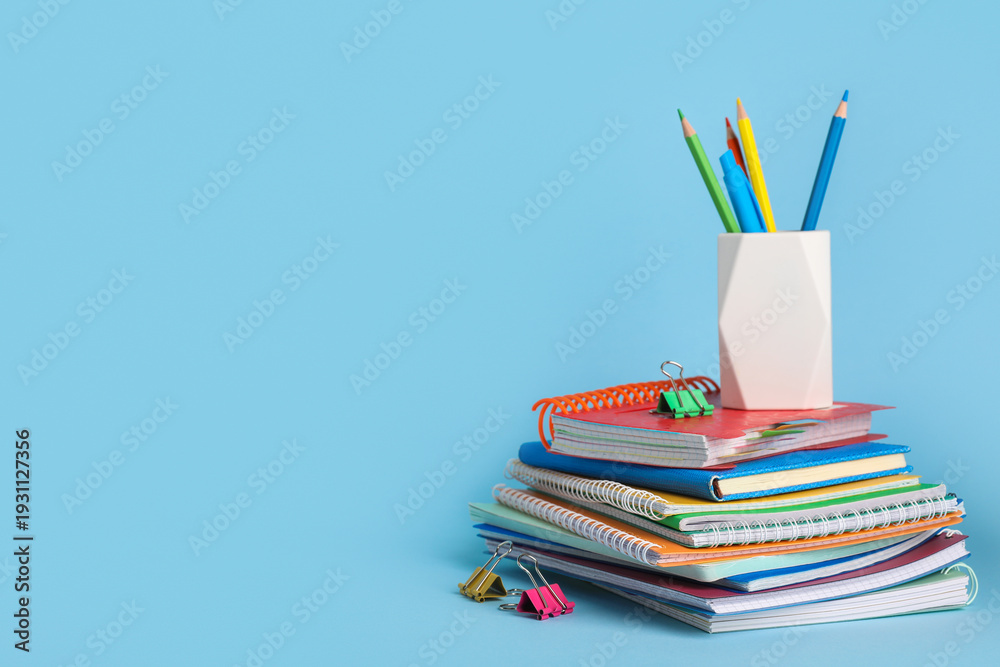 Fototapeta premium Stack of different notebooks with pencils holder on blue background