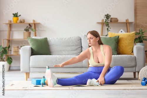 Young troubled overweight woman in sportswear with sport equipment stretching...