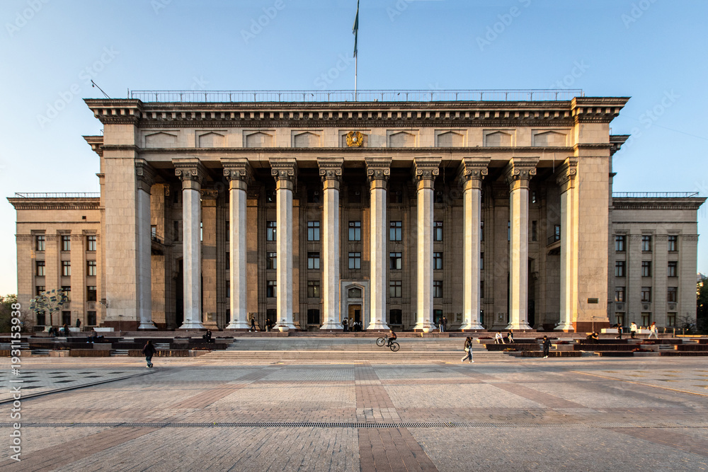 Naklejka premium Grand facade of the historical building with neoclassical columns and national flag. Almaty, Kazakhstan - October 04, 2024