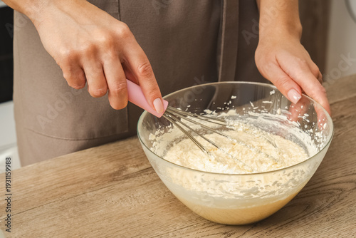 Close-up of a woman's hands holding a metal whisk and mixing cake batter. Photo.