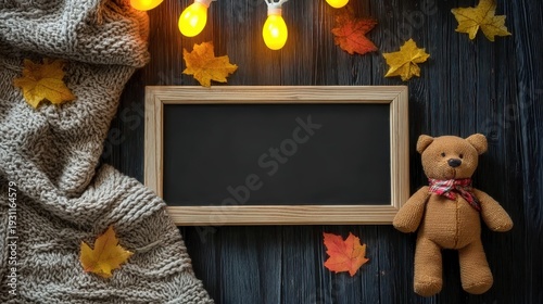 Flat lay pregnancy announcement concept for fall or winter, with black letter board, teddy bear, fairy lights, and blanket on wooden floor, ideal for social media or cards.