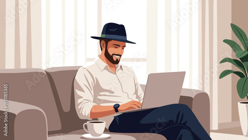 Smiling bearded man wearing a stylish hat sitting on a sofa and working on his laptop while enjoying a cup of hot coffee.