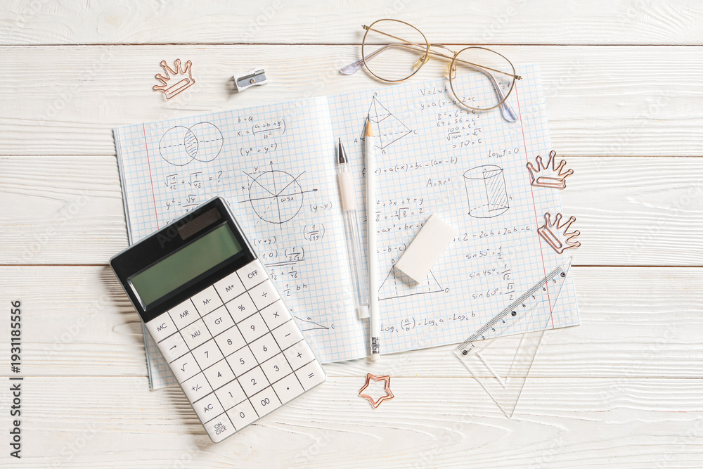 Naklejka premium Copybook with handwritten maths formulas, calculator and stationery on white wooden background