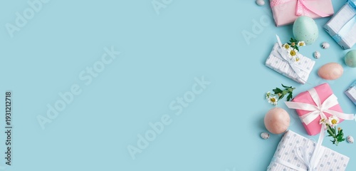 Painted Easter eggs, gift boxes and flowers on light blue background with space for text, top view
