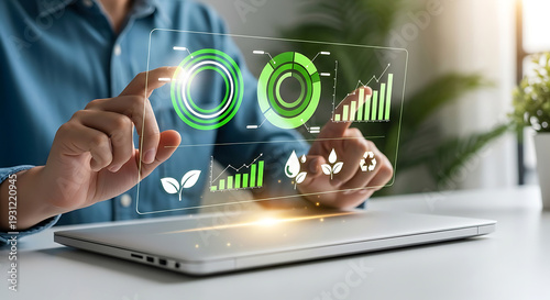 Person touching holographic green circular and bar charts with nature on laptop hand