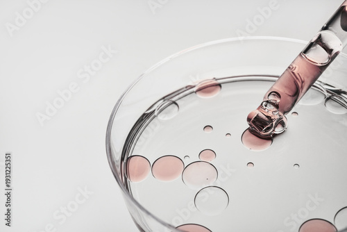 Dropper releasing cosmetic liquid and oil bubbles into clear dish on white background