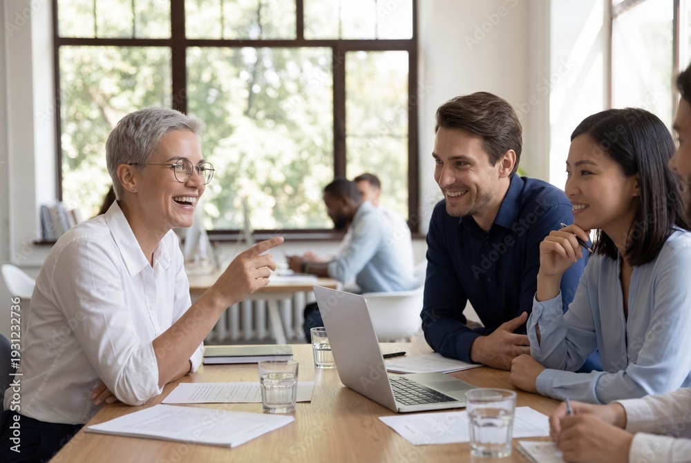 Fototapeta premium Cheerful diverse business team laughing and discussing project on laptop in modern office meeting