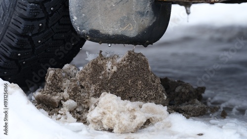 Foto Close-up of dirty slush and ice buildup on the ground next to a car tire and mudflap during winter