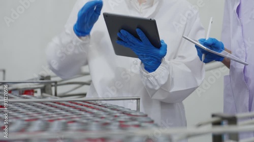 Canned food manufacturing industry, a quality control officer using a tablet to inspect products and check the accuracy of an automated conveyor machine in a processed food production line
