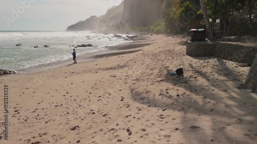 Asian woman and a child walking on a beach. The woman is holding the child's hand while running and laughing together. The beach is rocky and has a lot of rocks