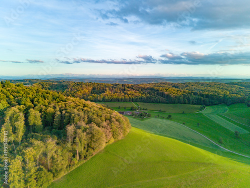 Slika na platnu Aerial view of rolling hills and forested landscape at sunset in a serene rural