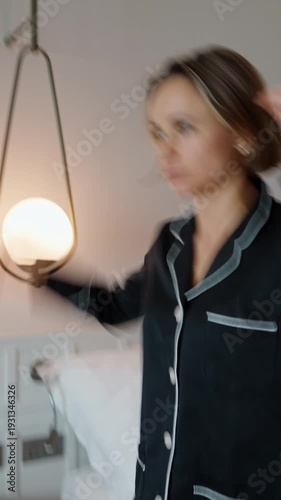 Woman standing in a modern room after waking up, holding her head as she experiences dizziness. Wearing pajamas, she appears disoriented and slightly unwell, suggesting fatigue, jet lag, headache, or