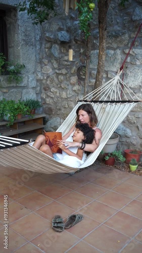 Mother reading a book to daughter in hammock at home patio