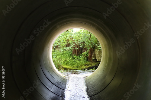Schilderij op canvas View through a round concrete tunnel carrying a stream beneath a road