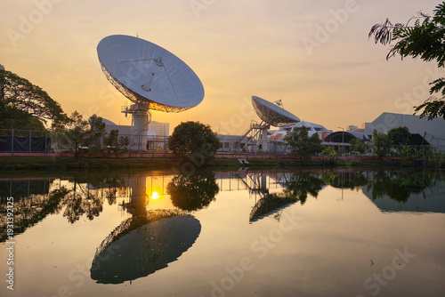 Big satellite dish antenna station with reflect on pond at sunrise