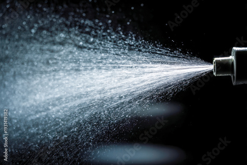 Spray from a nozzle dispersing fine mist droplets into the air against a dark background with detailed water particle texture