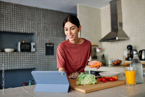 Wallpaper Mural Happy young latina woman having fun preparing food and looking for recipes online using a tabletor laptop in kitchen Torontodigital.ca