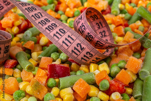 Pink measuring tape on frozen chopped vegetables mix, close up , weight loss concept