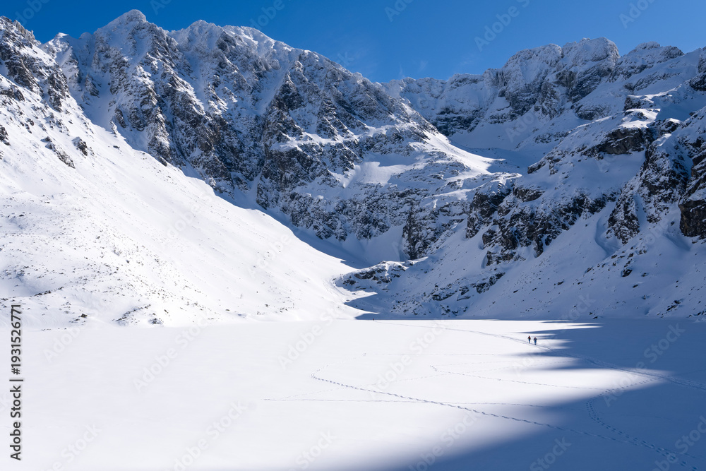 Obraz premium Czarny Staw Gasienicowy lake in Gasienicowa Dolina valley in winter in Tatra Mountains. Mountain winter landscape with frozen lake. High Tatras, Poland