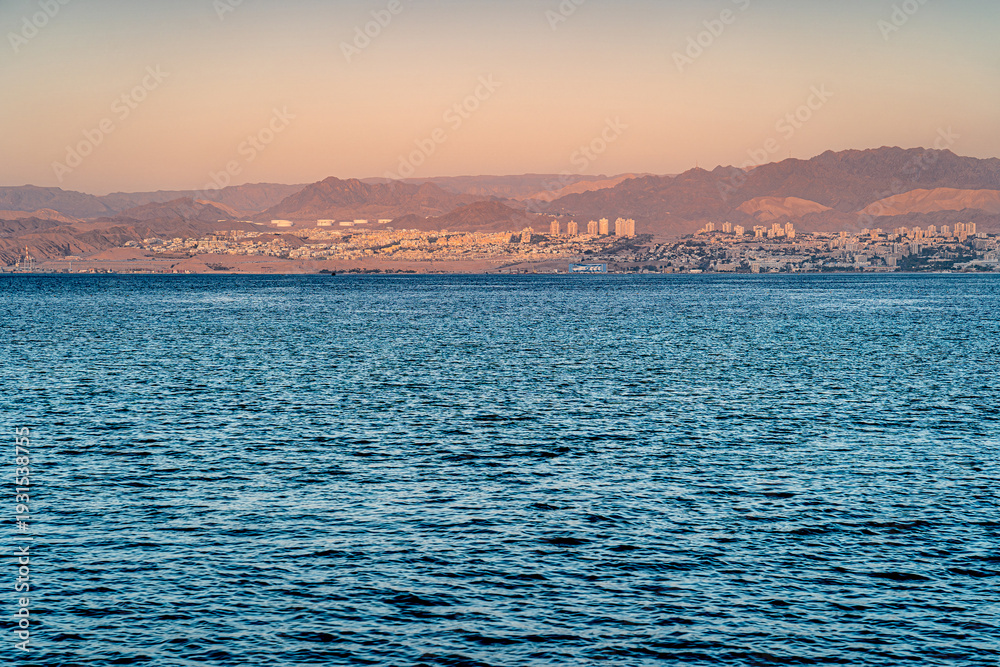 Obraz premium The coastal city of Eilat with the Israeli flag on the coast at sunrise.