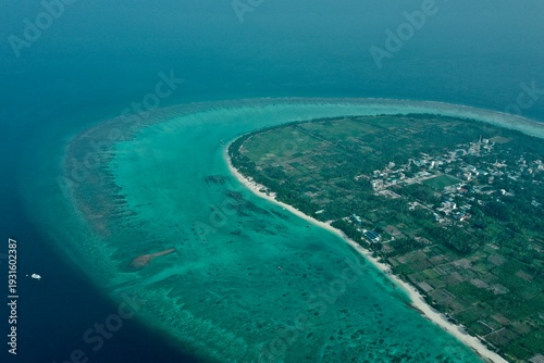 Obraz na płótnie Wide aerial shot of Thoddoo island showcasing the local village, dense palm forests, and an expansive turquoise coral reef surrounding the coastline in the Maldives