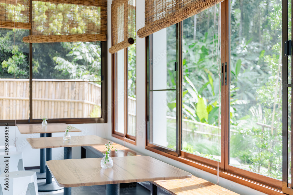 Fototapeta premium Minimalist Japanese Cafe Interior with Wooden Tables and Bamboo Blinds Overlooking Green Nature for Tranquility and Peace
