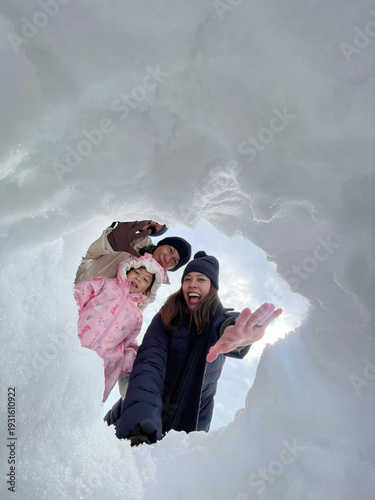 Joyful three-generation Asian family selfie portrait in Japan, featuring grandparents, parents, and a child smiling together through a snow hole, capturing a perfect winter vacation moment.