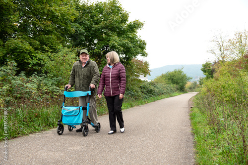 Elderly friends taking a walk in the park with help of walker to support and help move smiling and talking happy