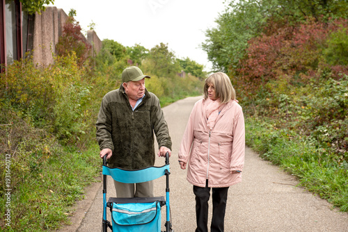 Elderly married couple taking a walk in the park with help of walker to support and help move