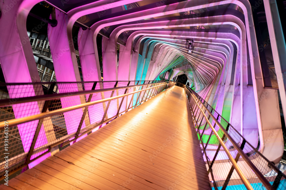 Fototapeta premium Wide Dynamic View of Phinisi Sudirman Pedestrian Bridge Interior with Neon LED Lighting at Night, Jakarta