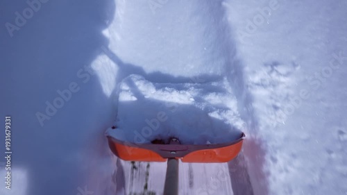 Point of view of snow removal with an orange shovel clearing fresh snow from a walkway on a sunny winter day outdoor seasonal maintenance concept, close up, slow motion