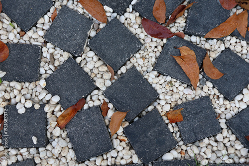 Black square stones and small white pebbles, with brown leaves fallen on the pathway
