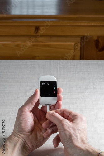 Close up of a man hands using a digital glucose meter to check blood sugar levels at home. Concept of diabetes management, medical self-testing, and healthcare monitoring for a healthy lifestyle.